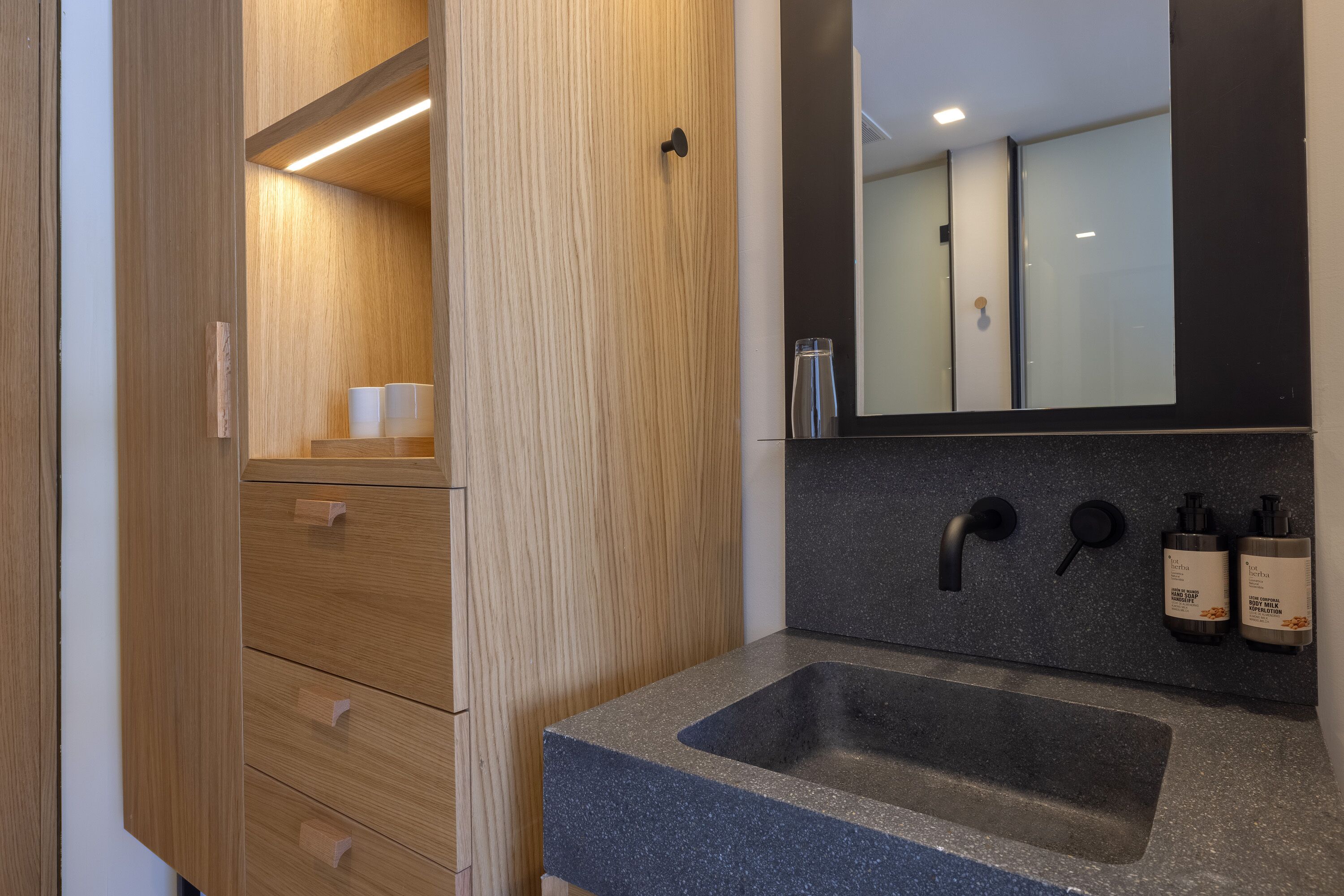 Een moderne badkamer met een houten wastafelmeubel, een wastafel met donker aanrechtblad en een spiegel boven de wastafel.