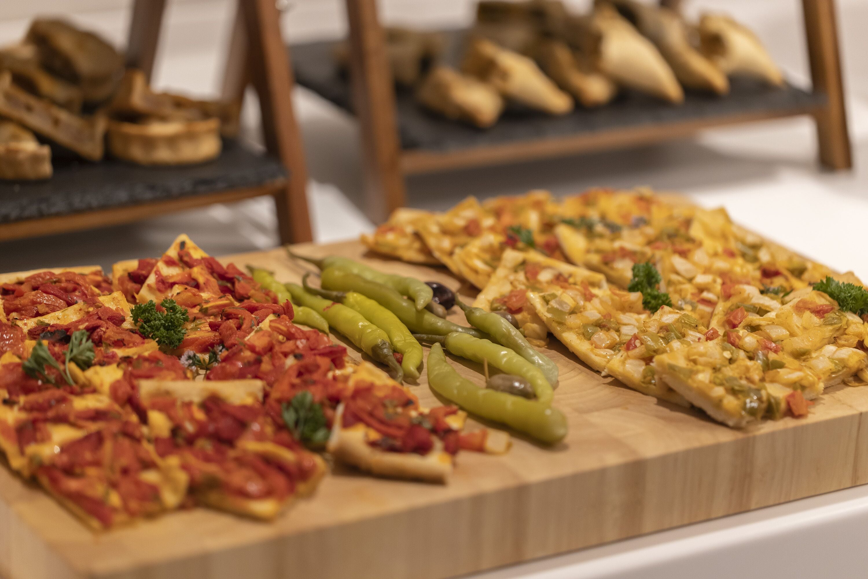 A wooden board with various pizzas and green peppers.