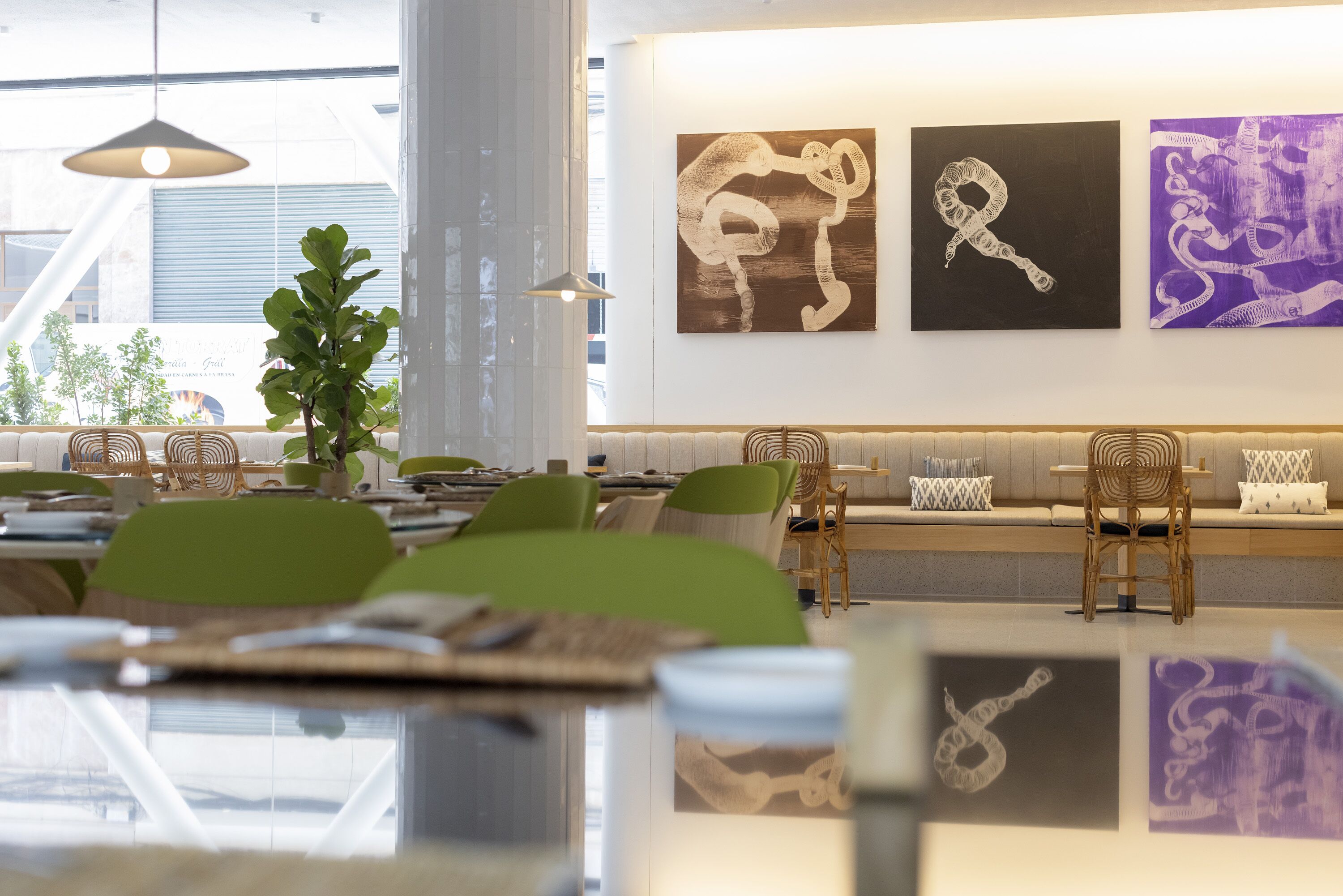 A modern interior with a long dining table, green chairs, and a seating area with a sofa and chairs. There are three artworks on the wall.