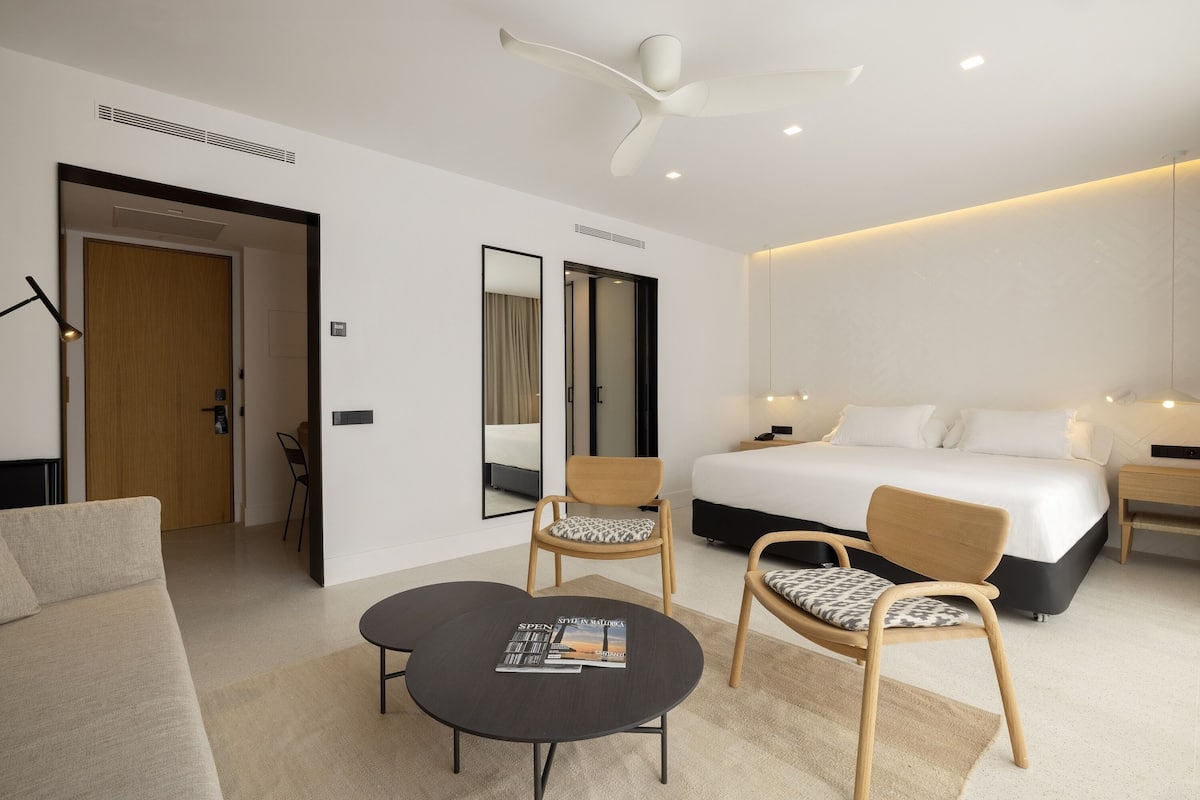 Een moderne hotelkamer met een groot bed, twee stoelen, een kleine tafel en een plafondventilator.
