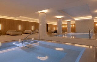 Un moderno vestíbulo de hotel con una amplia piscina interior, zonas de estar cómodas y un diseño espacioso.