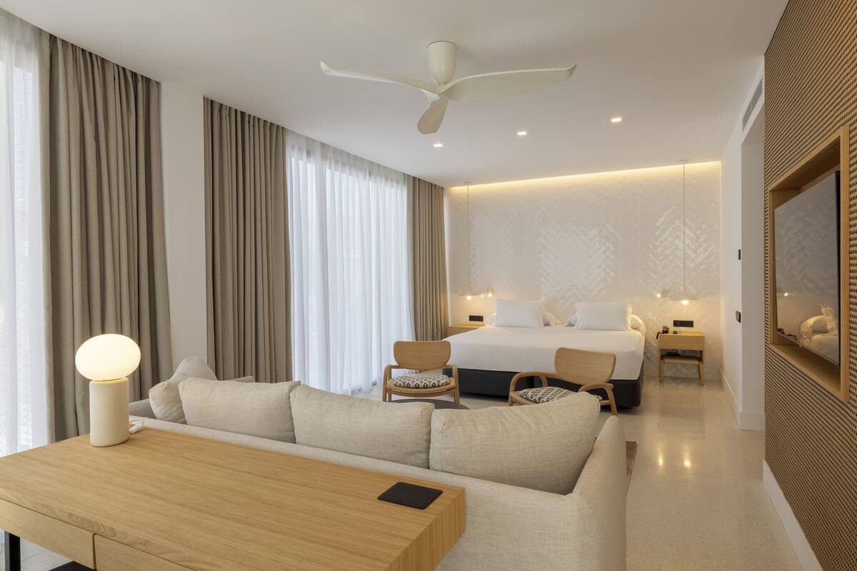 Een moderne hotelkamer met een bank, een bed, een bureau en een plafondventilator.