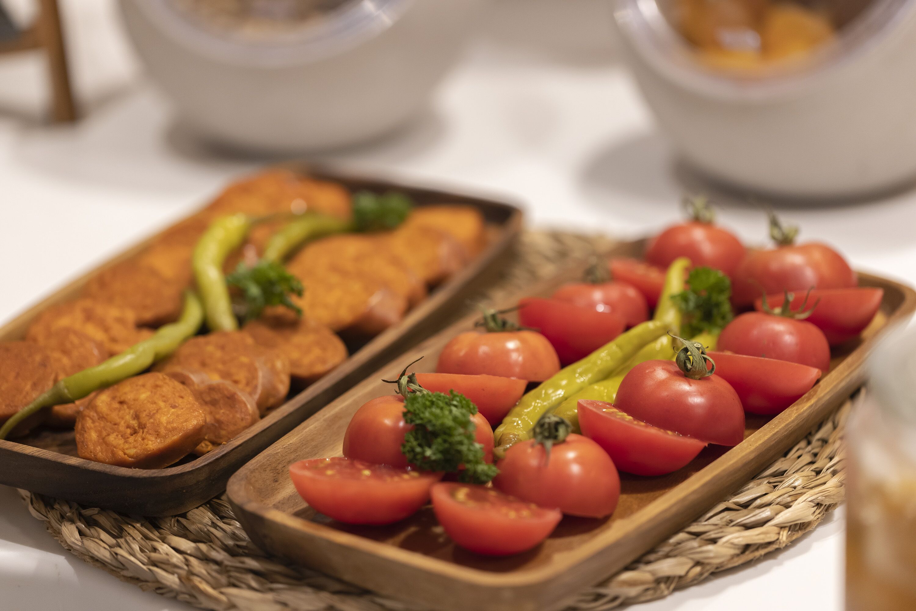Een houten dienblad met plakjes tomaat en groene paprika, en een houten dienblad met sneetjes brood.