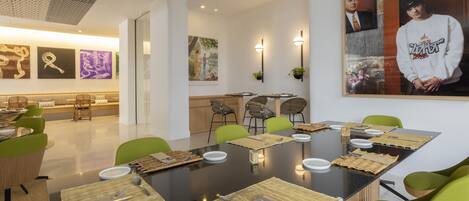 A modern dining area with a long table set for a meal, surrounded by green chairs.