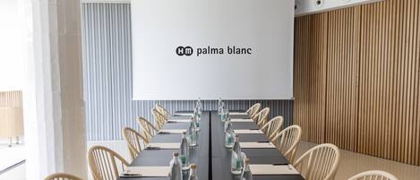 Un salón de conferencias con una larga mesa, sillas, una pantalla de proyector y botellas de agua.