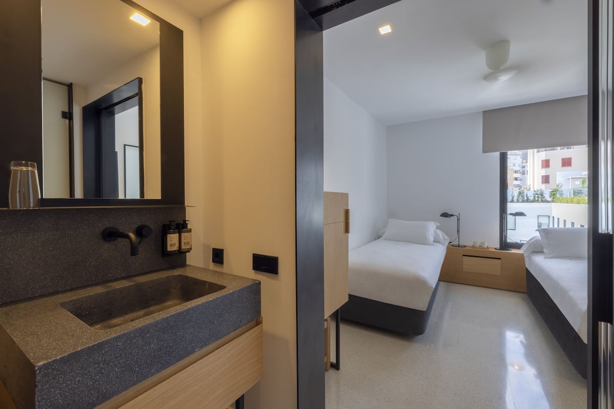 Een moderne hotelkamer met een grote spiegel, een granieten wastafel, twee bedden, nachtkastjes met lampen en uitzicht op de stad.