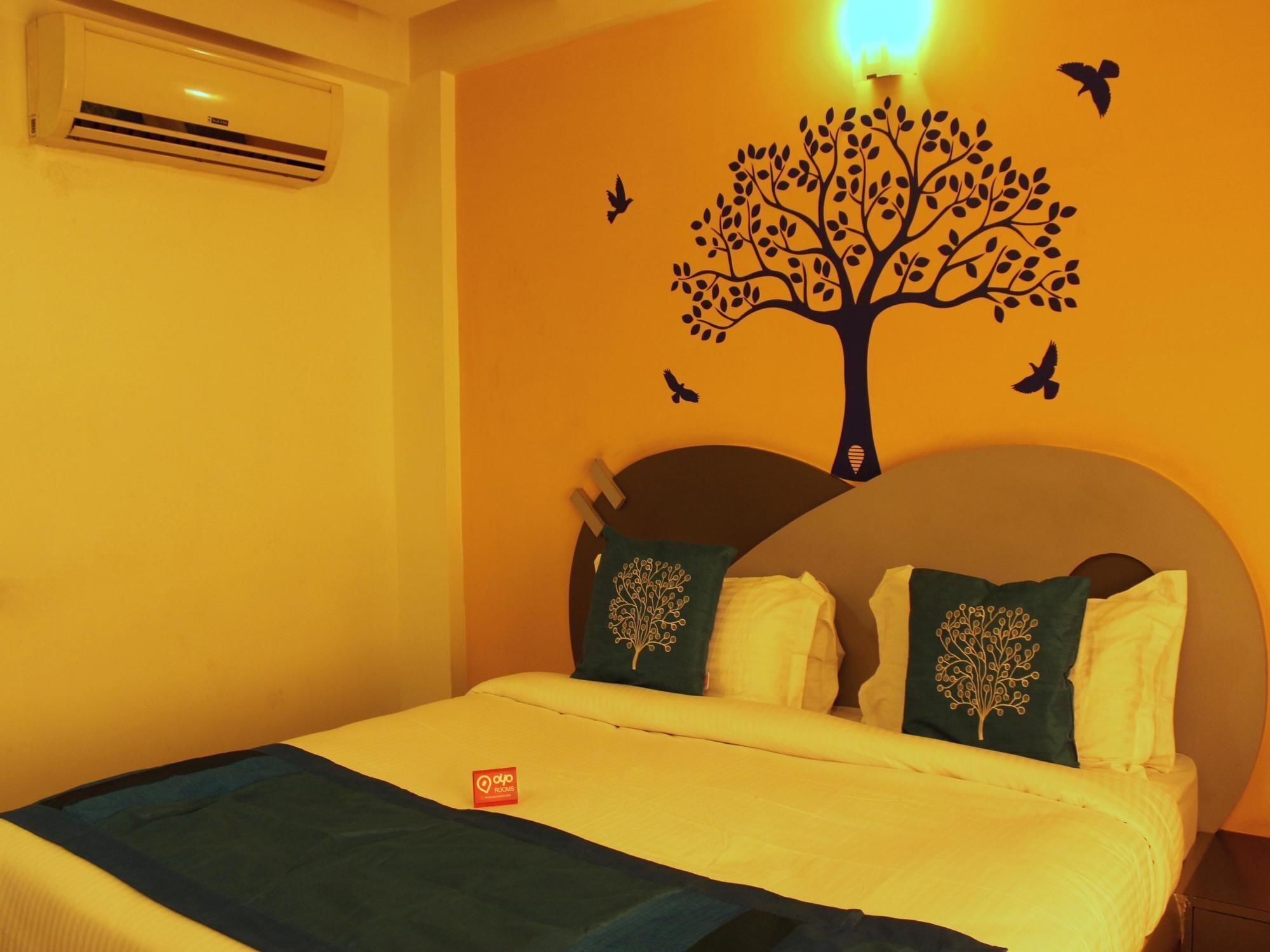 Une chambre d’hôtel avec un lit, un climatiseur fixé au mur et une décoration murale représentant un arbre avec des oiseaux.