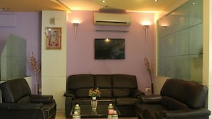 A living room with a black leather sofa, two armchairs, a coffee table with decorative items, and a flat-screen TV mounted on the wall. - OYO Rooms Inside Udaipole (Udaipur)
