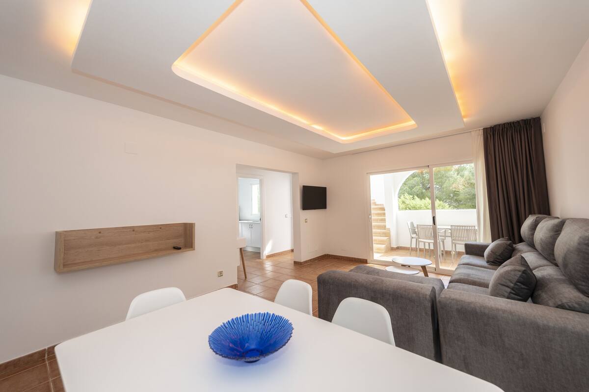 Een moderne woonkamer met een bank, een eettafel en een aan de muur bevestigde televisie.