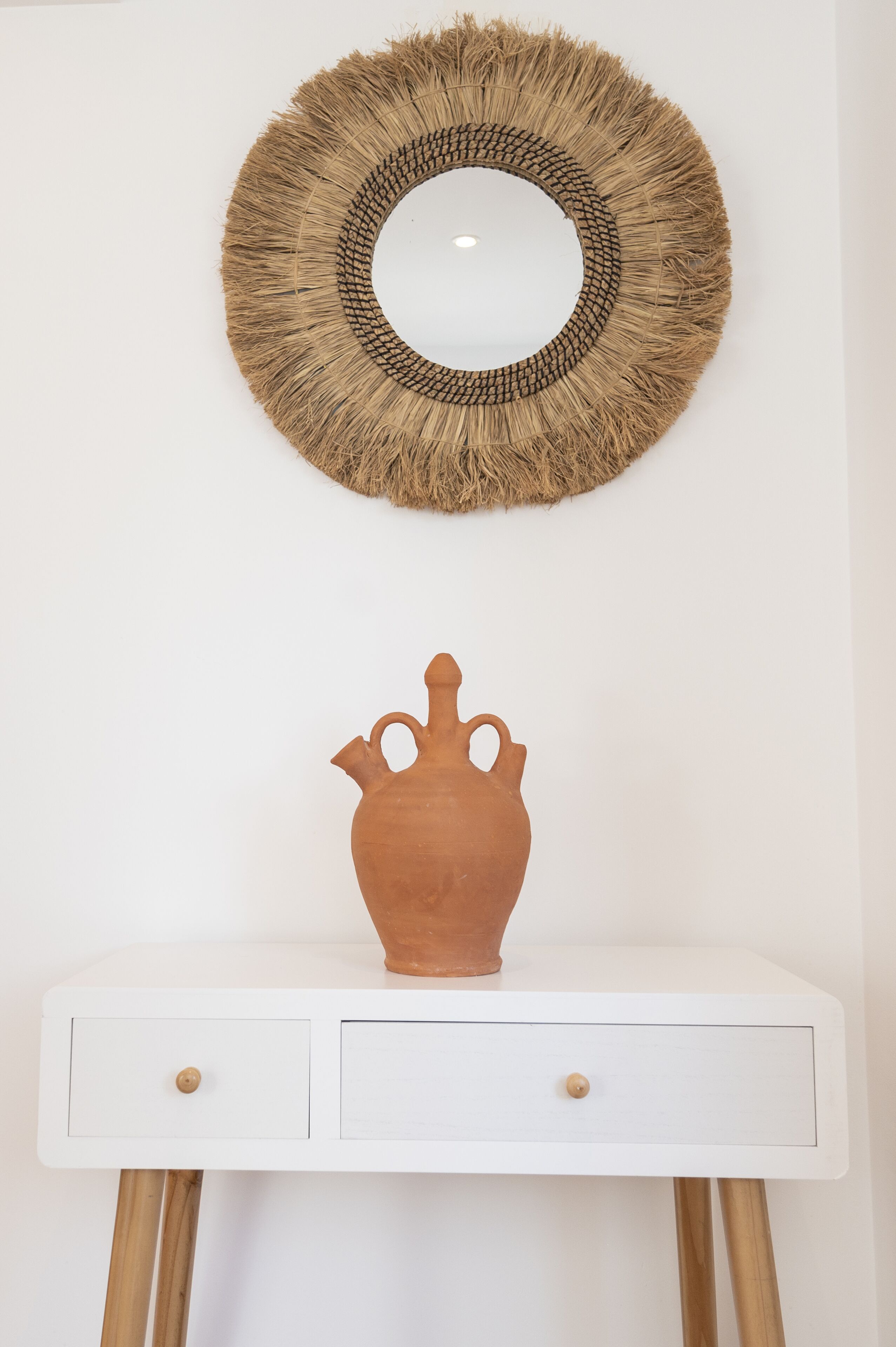 Een witte tafel met twee lades en een terracotta pot erop.