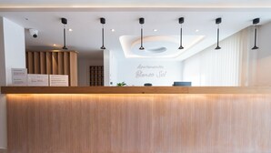 Uma receção com bancada de madeira, design moderno no teto e um letreiro que diz 'Apartamentos Blanco Sol'.