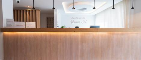 A reception desk with a wooden finish, a modern ceiling design, and a sign reading 'Apartamentos Blanco Sol'.