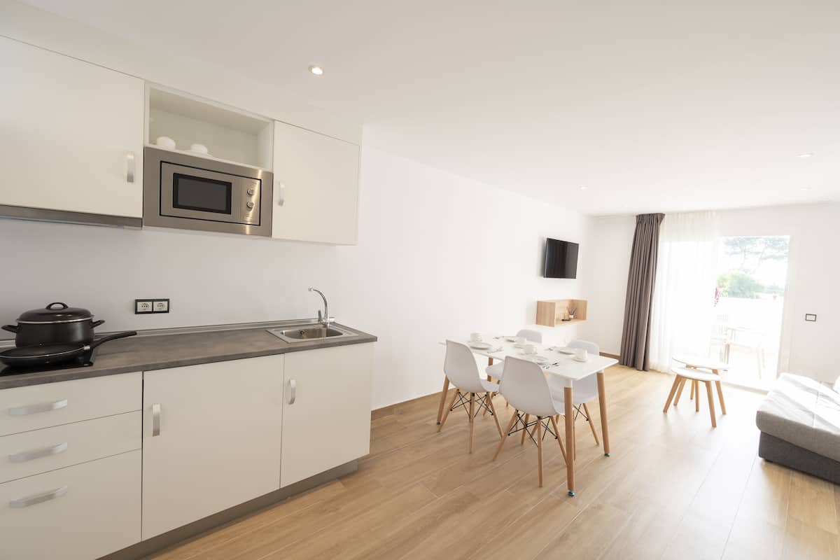 Een moderne keuken met een magnetron, fornuis en spoelbak. Er is een eethoek met een tafel en stoelen.