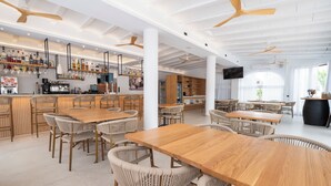Um restaurante espaçoso com tetos altos, mesas de madeira, cadeiras de vime e um bar com prateleiras cheias de garrafas e copos.