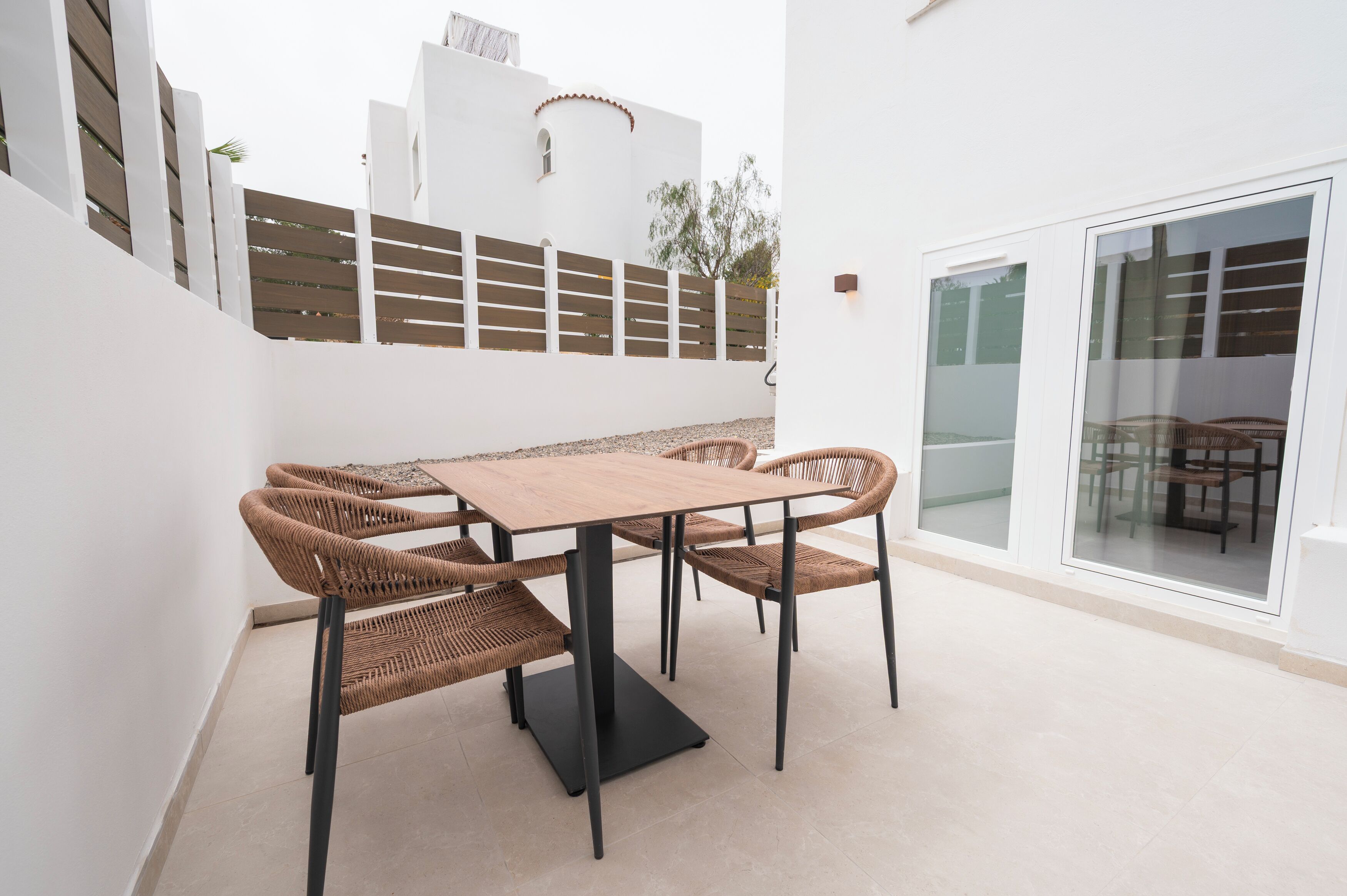 A patio with a table and chairs, a white wall, and a sliding glass door.