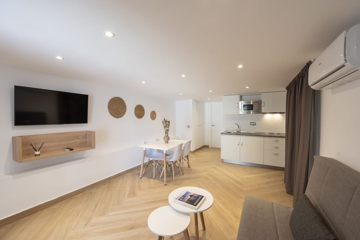 Een moderne woonkamer met een flatscreen televisie, een eethoek met een tafel en stoelen, een keuken met een magnetron, en een bank.