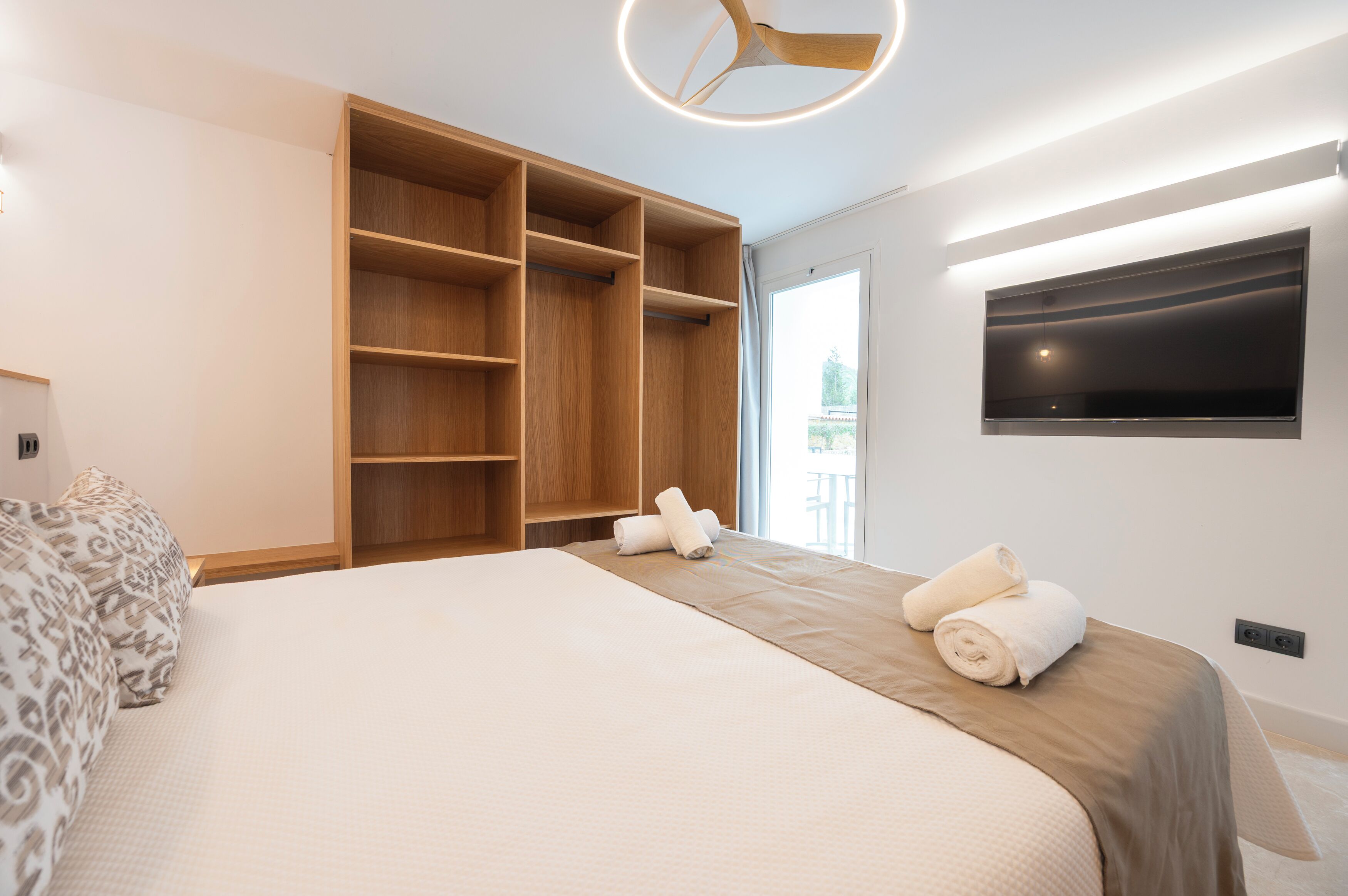 A bedroom with a bed, built-in wooden shelving, a flat-screen TV, and a ceiling fan.