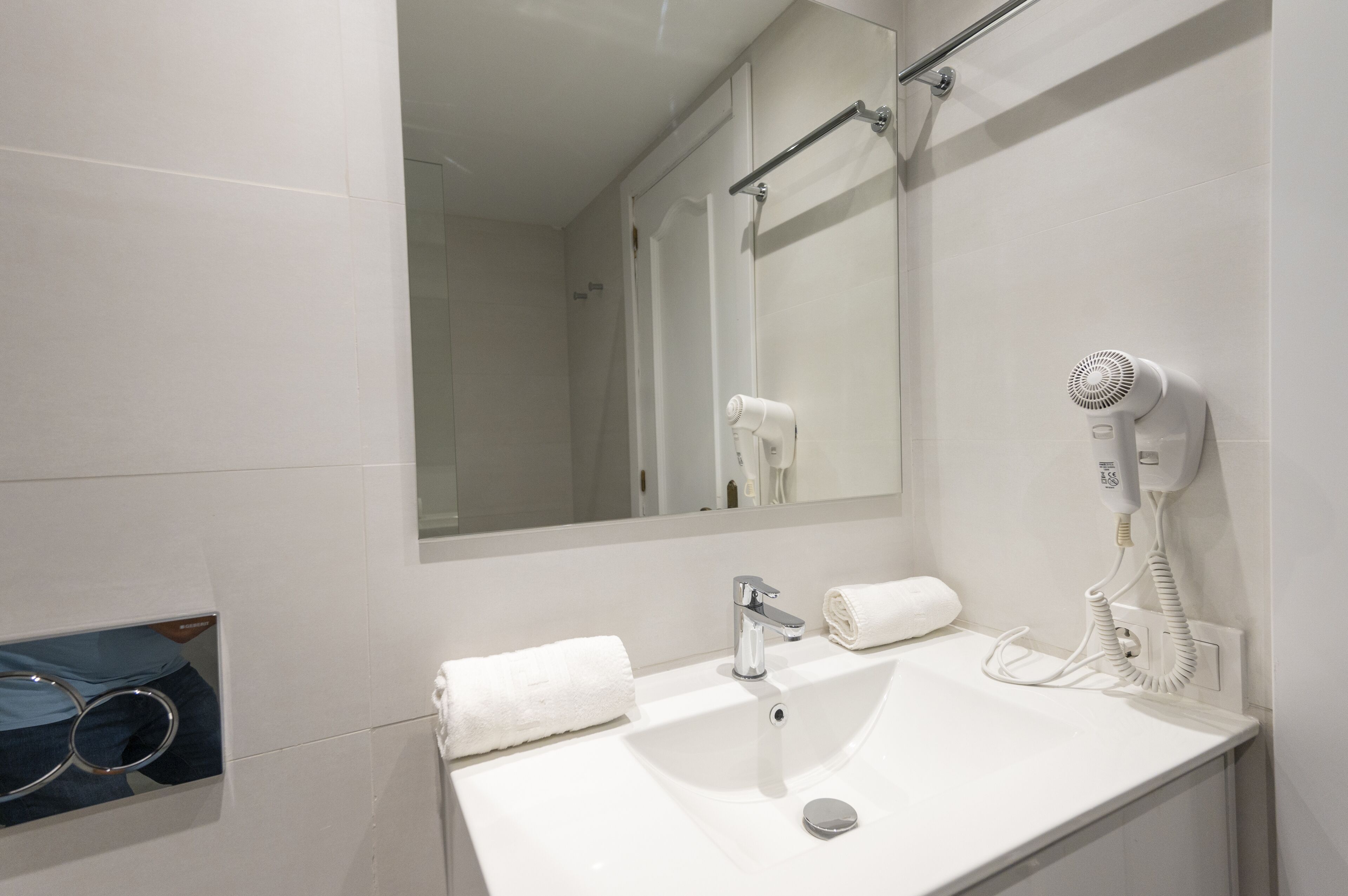 Une salle de bain moderne avec un lavabo blanc, un miroir, un porte-serviettes et un sèche-cheveux.