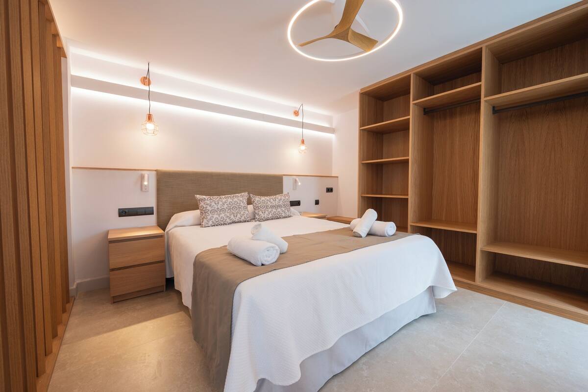 Een moderne slaapkamer met een groot bed, een houten hoofdbord, nachtkastjes en ingebouwde houten planken.