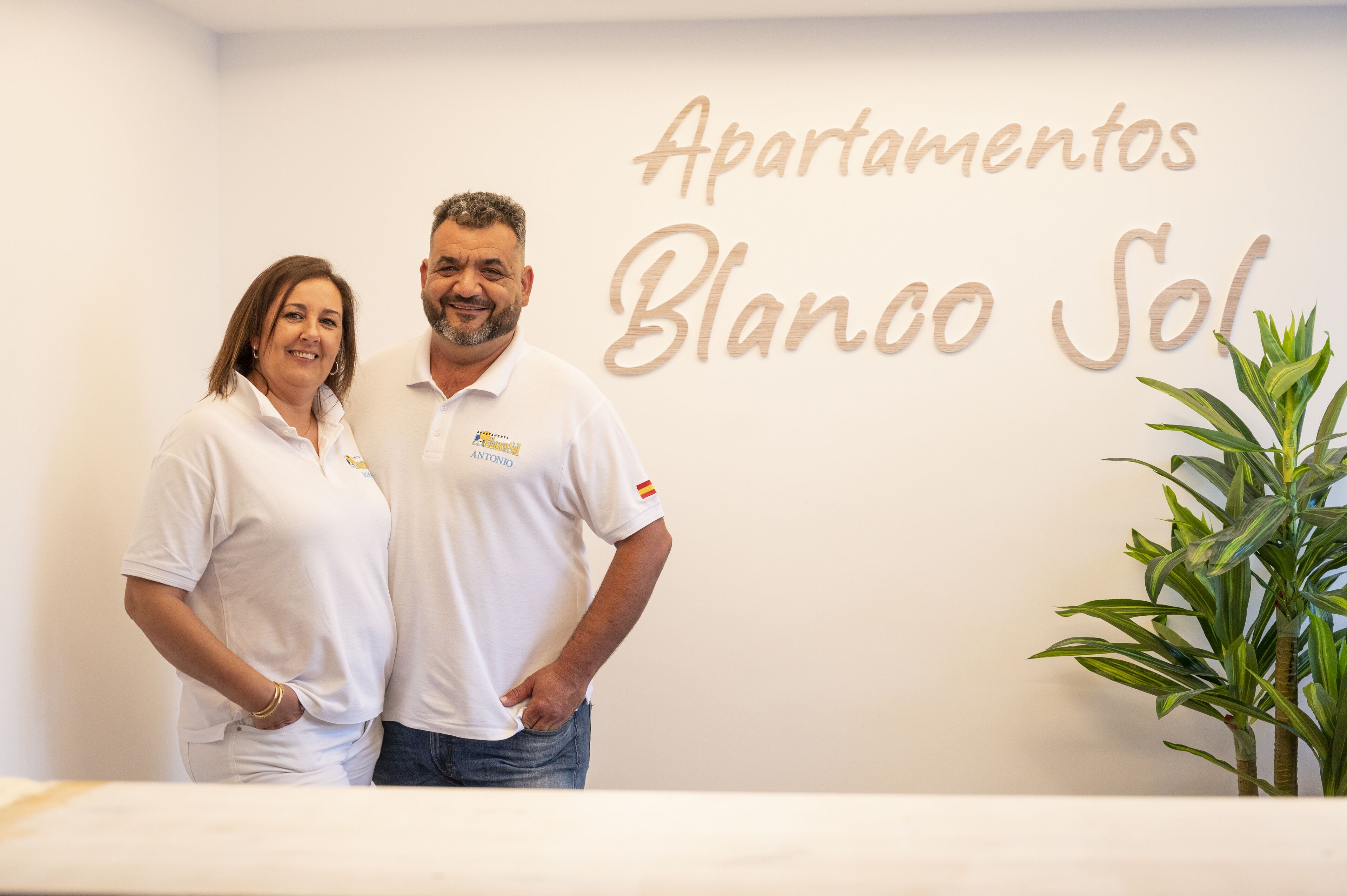 Dos personas de pie frente a un muro con el texto "Apartamentos Blanco Sol".