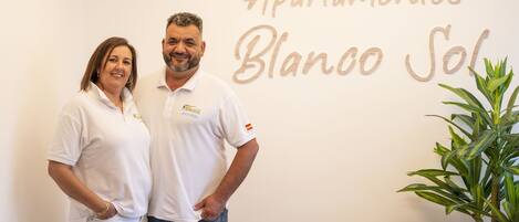 Dos personas de pie frente a un muro con el texto "Apartamentos Blanco Sol".