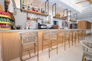 A bar area with wicker chairs, shelves with bottles and glasses, and a coffee machine.