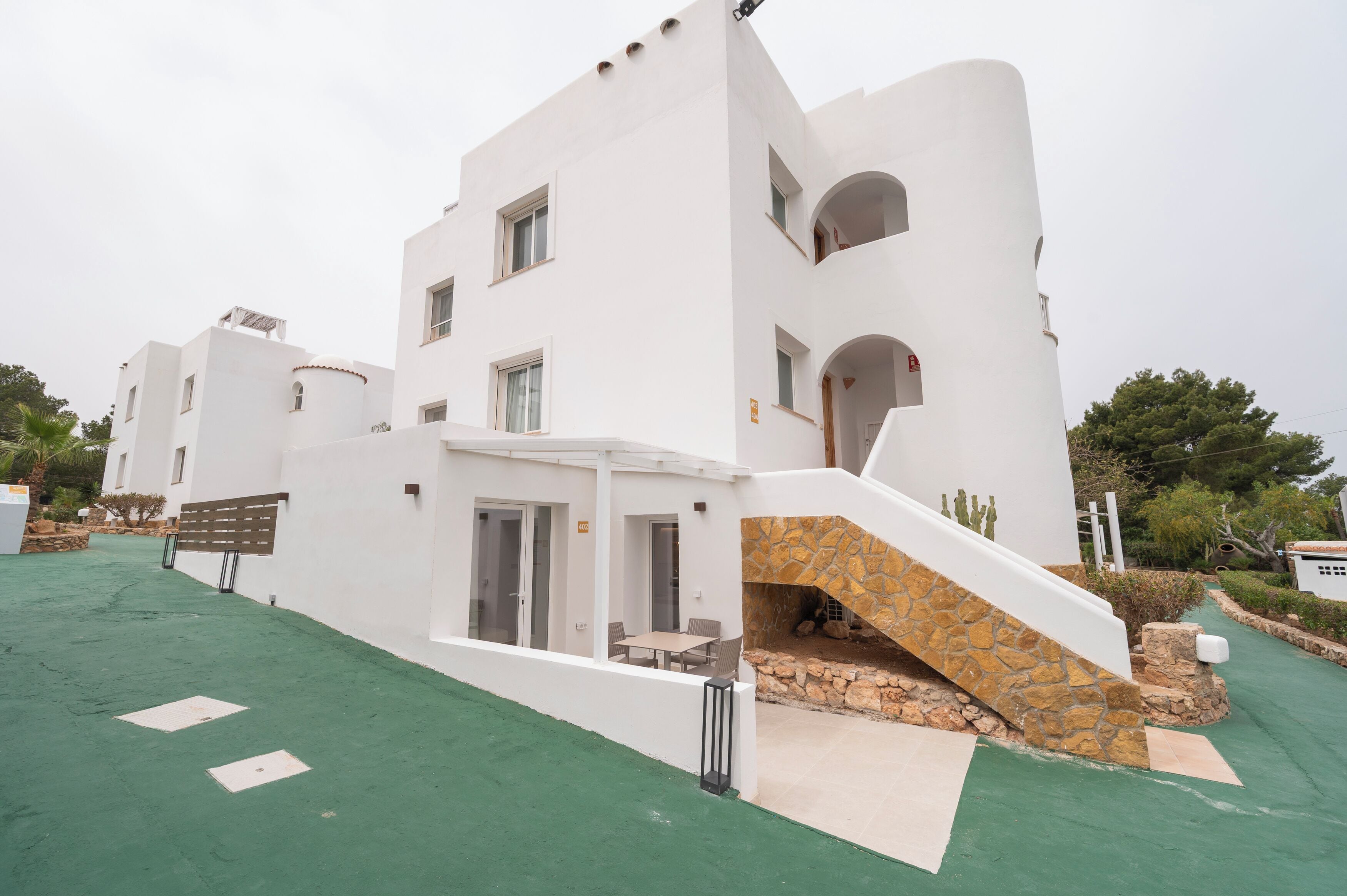 A modern white building with a stone staircase, a covered patio, and a view of the surrounding greenery.