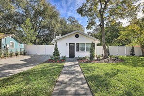A single-story house with a front yard, a paved walkway, and a small garden with red flowers. - Chic Home w/ Fire Pit & Patio, Walk to Lake! (Mt Dora)