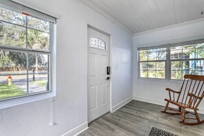 A room with a white door, large windows, a rocking chair, and a patterned rug. - Chic Home w/ Fire Pit & Patio, Walk to Lake! (Mt Dora)