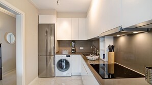 A modern kitchen with a stainless steel refrigerator, built-in washing machine, and a black induction cooktop. - 'Vilamoura Apartment 3 bedroom' with Sea View, Terraces, Shared Pool & Wi-Fi (Vilamoura)