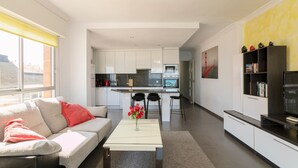 A modern living room with a sofa, coffee table, and a kitchen in the background.