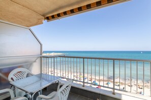 A balcony with a table and chairs, overlooking a beach with people and umbrellas.