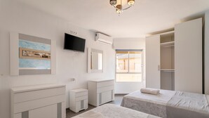 A hotel room with two beds, a TV, a painting, a wardrobe, and a window with a view.