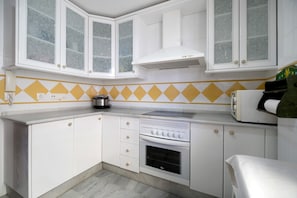 Une cuisine avec des meubles blancs, une cuisinière et un four à micro-ondes.