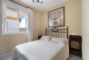 Une chambre à coucher avec un lit, une table de chevet, un tableau accroché au mur et une fenêtre avec des rideaux.