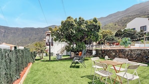Une pelouse bien entretenue, agrémentée de mobilier d’extérieur, d’un arbre et offrant une vue sur les montagnes en arrière-plan.
