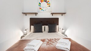Un lit bien fait, avec une tête de lit marron, deux lampes de chevet et une œuvre d’art accrochée au mur au-dessus.
