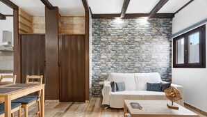 Une pièce avec un mur en pierre, des meubles en bois, un canapé blanc et une fenêtre.