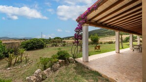 Un patio abrité offrant une vue sur un jardin aménagé et sur des collines lointaines.