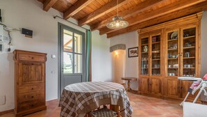 Une cuisine avec des meubles de rangement en bois, une table à manger recouverte d’une nappe à carreaux et un luminaire suspendu.