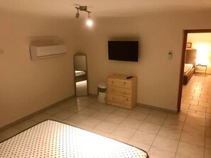 Een slaapkamer met een bed, een dressoir, een spiegel, een televisie aan de muur en een deur naar een andere kamer.