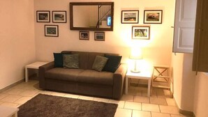 Een woonkamer met een bank, een klein tafeltje, een lamp en lijstjes met foto's aan de muur.
