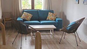 Un salon avec un canap é bleu, deux coussins à motifs, une table basse blanche et deux fauteuils en osier.