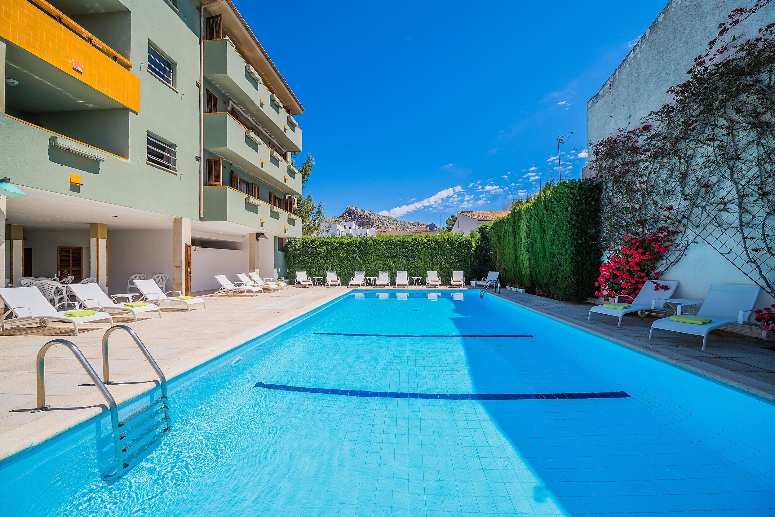 Une piscine avec des chaises longues, un bâtiment doté de balcons et un ciel dégagé.
