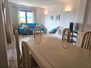 Spiseområde med et træbord og stole, en blå sofa og udsigt gennem et vindue.