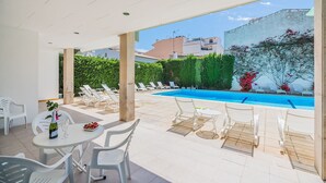 Un espace aménagé au bord de la piscine, avec des chaises longues, une table sur laquelle se trouvent une bouteille et un verre, et une vue sur la piscine et la végétation environnante.