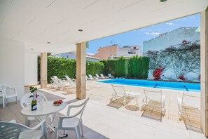A poolside area with lounge chairs, a table with a bottle and glass, and a view of the pool and surrounding greenery.