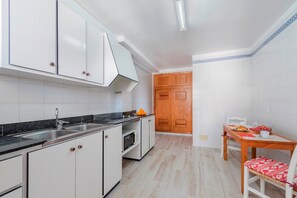 A kitchen with white cabinets, a black countertop, a wooden door, and a dining table with red cushions.