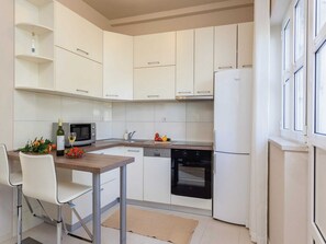 A modern kitchen with white cabinets, a microwave, a dishwasher, and a refrigerator. - Apartments Ankora (Dubrovnik)
