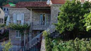 A stone house with a red-tiled roof, a balcony with white railings, and a view of a mountainous landscape. - Apartments Ankora (Dubrovnik)
